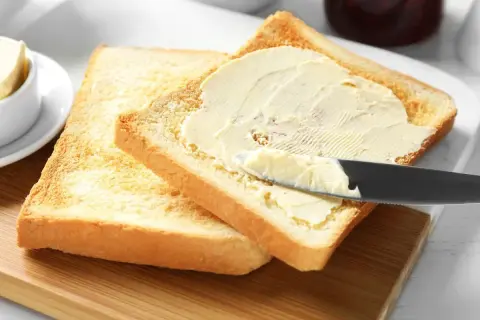 Na desce leżą dwa tosty. Na jednym z nich nóż rozsmarowuje masło. Ile gram ma kromka chleba tostowego?