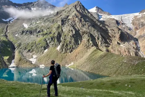 Un randonneur admire un lac turquoise lors d'un trek en Autriche, avec des montagnes imposantes en arrière-plan.