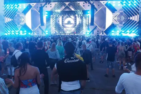 Tłum ludzi na festiwalu Sunrise w Kołobrzegu, podziwiający ogromną scenę z efektami świetlnymi.