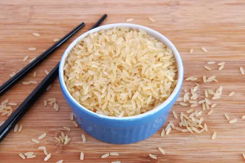 Ein blauer Napf mit hellem Reis, daneben schwarze Stäbchen. Der Unterschied Basmati und Parboiled Reis wird hier visuell dargestellt.