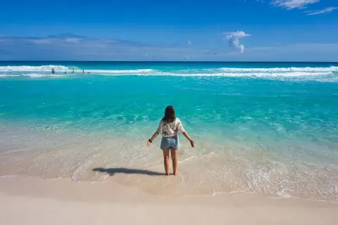 Frau steht im türkisfarbenen Meer, genießt das warme Wetter im Mexiko im Oktober. Der Strand ist sandig, das Wasser klar.