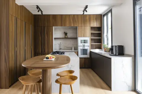 Cuisine moderne aux finitions boisées, conçue par un architecte d'intérieur. Table ovale en bois, tabourets, îlot central en marbre, et électroménagers intégrés.