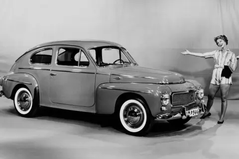 En glad kvinna poserar bredvid en klassisk Volvo PV 444.