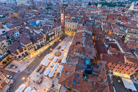 Vista aerea di piazza Erbe a Verona, con i suoi edifici storici, la torre e i tavolini all'aperto.