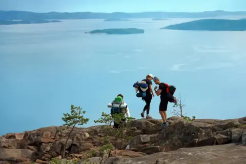 Vandrare med ryggsäckar njuter av utsikten över den blåa skärgården vid Höga kusten.