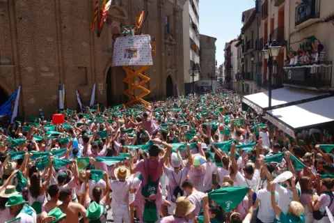 Multitud celebra el programa fiestas Huesca, agitando pañuelos verdes. Un cartel anuncia "25".