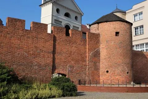 Kamienna baszta obronna, znana jako baszta Dorotka, z charakterystycznym stożkowym dachem, otoczona ceglanym murem.