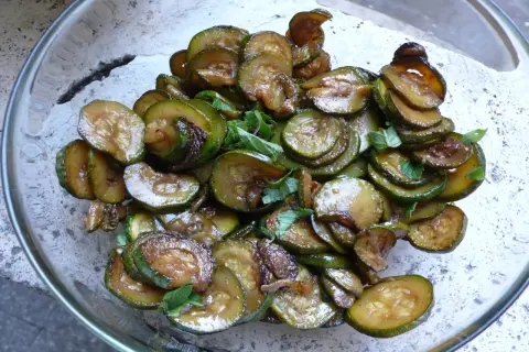 Zucchine alla scapece, fritte e condite con aceto e menta, in una ciotola di vetro.