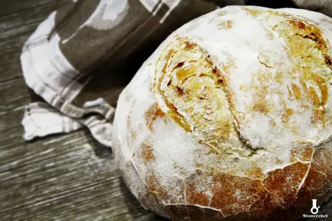 Świeżo upieczony bochenek chleba na drożdżach, oprószony mąką, leży obok lnianej ściereczki. Idealny przepis na chleb na drożdżach.