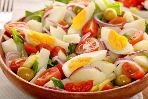 Ensalada de patatas de verano con huevo duro, tomates, aceitunas y cebolla morada en un cuenco de madera.
