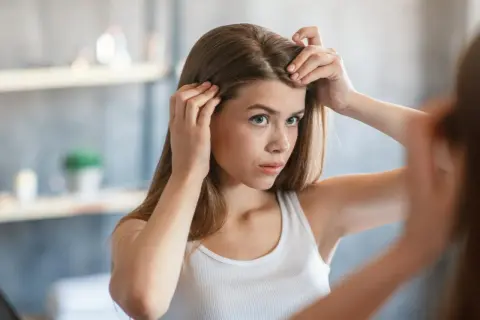 Junge Frau prüft im Spiegel ihre Haare und fragt sich, wie viel wachsen Haare im Monat.