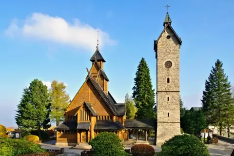 Drewniany kościółek i kamienna wieża z zegarem, jedne z głównych karpacz atrakcje w okolicy, otoczone zielenią.