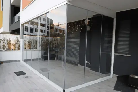 Veranda balcone con vetrate scorrevoli, luci decorative e piante. Spazio moderno e luminoso.