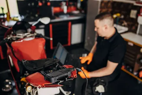 Mecánico con guantes naranjas usa un portátil para ver cómo se puede reprogramar una moto roja.