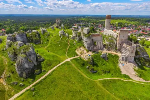 Ruiny zamków na wapiennych skałach w parku krajobrazowym Orlich Gniazd, otoczone zielonymi wzgórzami i lasami.