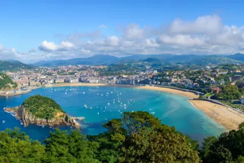 Widok na zatokę La Concha w San Sebastián. Widać miasto, plażę, góry i liczne łodzie na wodzie. Idealne miejsce na loty widokowe.