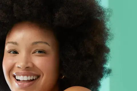 Rostro sonriente de mujer con afro, piel radiante. Evita la glicerina, es mala para la piel.