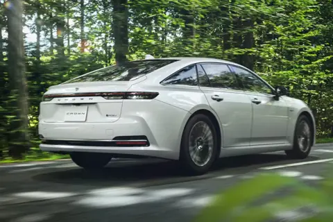 Biały Toyota Crown sunie przez zielony las.