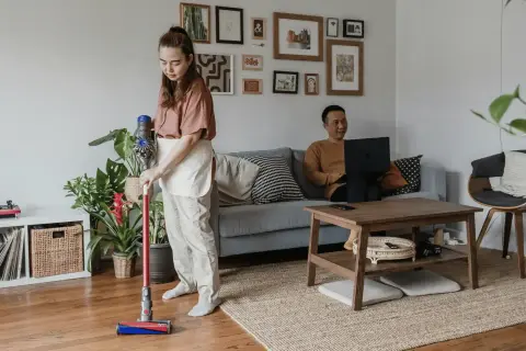 Kobieta sprząta mieszkanie odkurzaczem Dyson, podczas gdy mężczyzna pracuje na laptopie. Zastanawiasz się, który Dyson wybrać?
