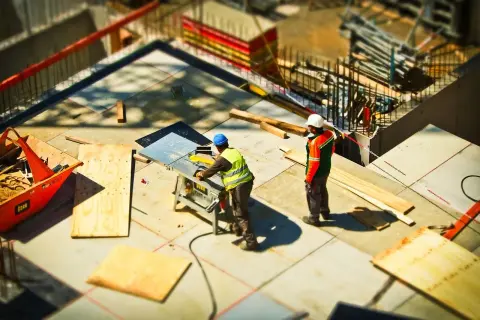 Obreros trabajan en una obra, uno usa una sierra eléctrica y el otro observa. Se preparan materiales para juntas de dilatación.
