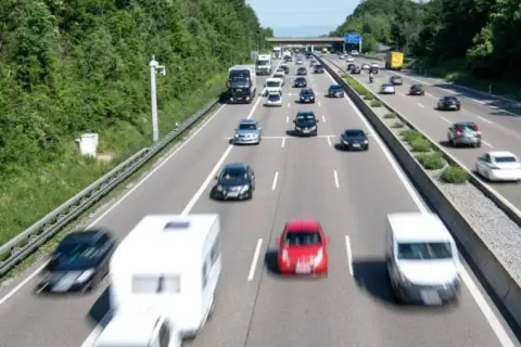 Autobahn mit vielen Autos und einem Wohnwagen. Ein Schild am Horizont deutet das ende autobahn schild an.