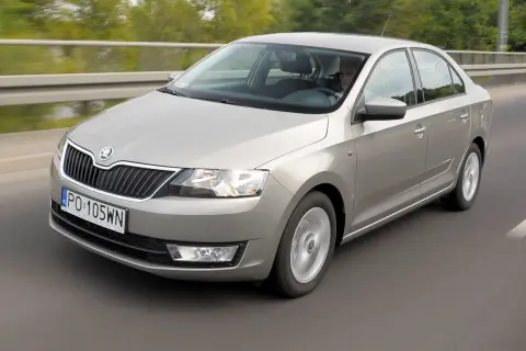 Srebrna Skoda Rapid jedzie po drodze. Kierowca jest widoczny za kierownicą. Wiele osób szuka skoda rapid opinie przed zakupem.