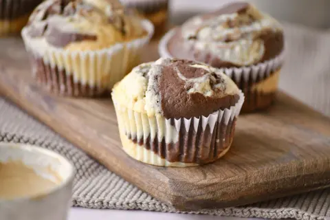 Zwei leckere Marmor Muffins auf einem Holzbrett, daneben eine Tasse Kaffee.