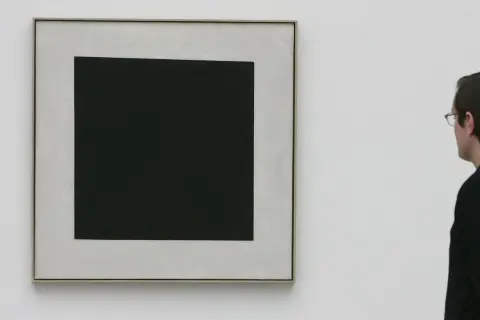 Ein Mann betrachtet ein schwarzes Quadrat auf hellem Grund. Die schlichte Komposition lässt Raum für Interpretationen, die schwarzes Quadrat Bedeutung.