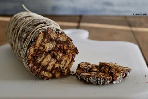 Salame dolce con cacao, un goloso rotolo di biscotti e cioccolato, legato con spago e cosparso di zucchero a velo.