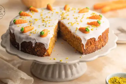 Ein saftiger karottenkuchen mit cremigem frosting, dekoriert mit kleinen Marzipan-Karotten und gehackten Pistazien.