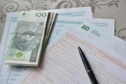 Stos papierów z ZUS, pieniądze i długopis sugerują, jak obliczana jest emerytura.