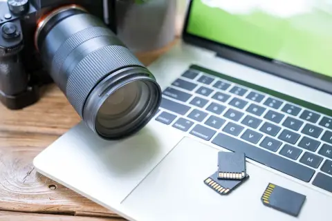 Aparat fotograficzny i karty pamięci leżą obok laptopa, gotowe do akcji. Dowiedz się, jak zgrać zdjęcia z aparatu na laptop.