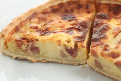 Un trozo de quiche de verduras con trocitos de bacon, horneado hasta dorarse.