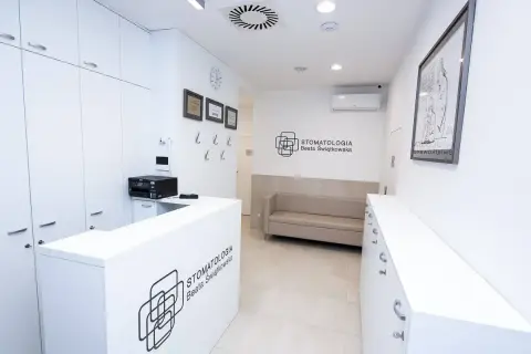 Nowoczesne wnętrze recepcji stomatologicznej z białym lady, kanapą i logo kliniki.