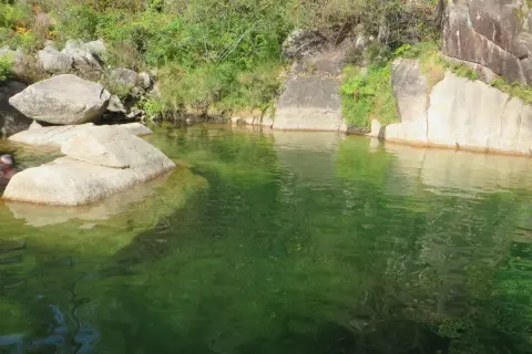 Un hombre se baña en la poza de agua verde de la corga da fecha, rodeada de rocas y vegetación.