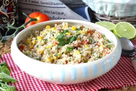 En skål med färgglad quinoa sallad med majs, tomat och persilja, garnerad med limeklyftor.