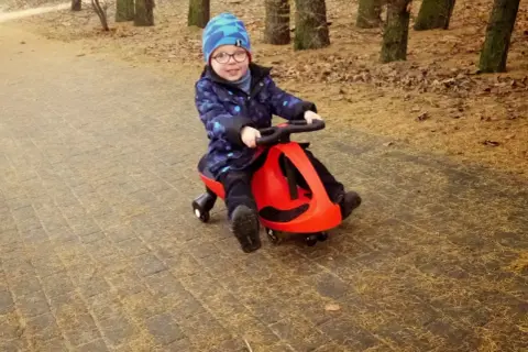 Uśmiechnięty chłopiec w czapce jedzie na czerwonym twistcarze. Od jakiego wieku można zacząć zabawę? Odpowiedź znajdziesz na blogu!