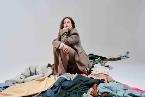Donna pensierosa seduta su un cumulo di vestiti, simbolo del consumismo del brand fast fashion.