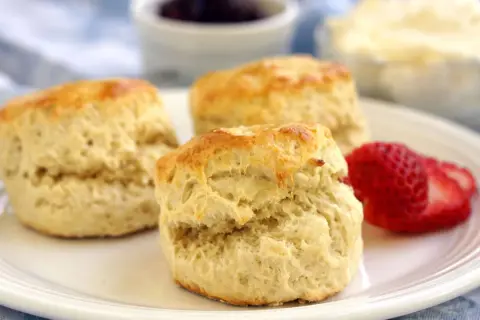 Tre fluffiga scones, ett perfekt scones grundrecept, serveras med jordgubbar och grädde.