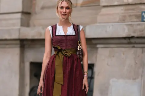 Frau mit Dirndl und einer grünen Schürze, die sie elegant um die Taille gebunden hat.