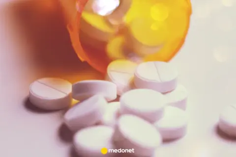 Białe tabletki, w tym lorazepam, wysypują się z pomarańczowego pojemnika.