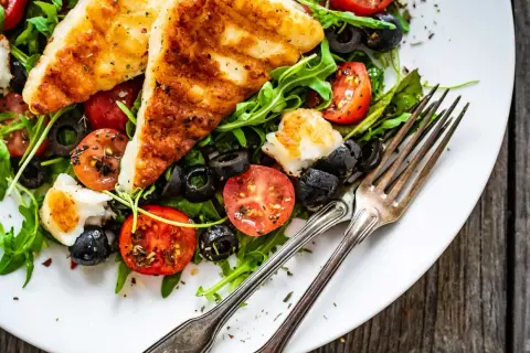 Pyszna sałatka z grillowanym halloumi, pomidorkami koktajlowymi i czarnymi oliwkami na rukoli. Idealna na lekki posiłek.