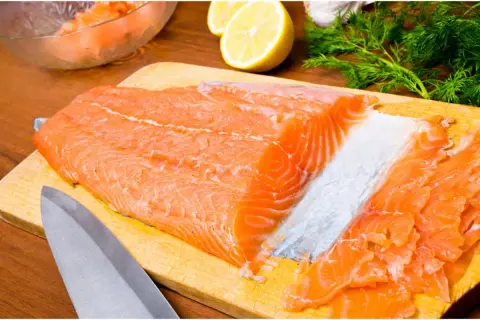 Un beau filet de truite saumonée prêt à être transformé en gravlax, avec du citron, de l'aneth et de l'ail en arrière-plan.