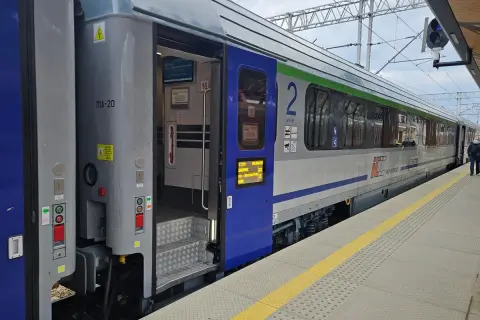 Eurocity train z otwartymi drzwiami na peronie. Widoczne schody, oznaczenia wagonu i fragmenty wnętrza.