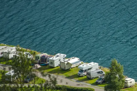 Un garaje al aire libre con varias caravanas y autocaravanas aparcadas junto a un lago azul.