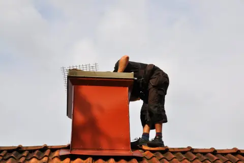 Pracownik na dachu wykonuje uszczelnianie komina, dbając o jego szczelność i bezpieczeństwo.