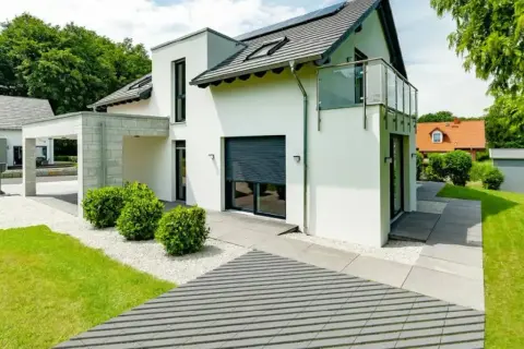 Nowoczesna elewacja wokół drzwi wejściowych z białym tynkiem, kamienną wiatą i zielenią.