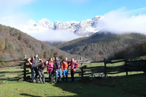 Grupo de senderistas posa junto a un cercado de madera en la ruta Soto de Sajambre-Vegabaño, con montañas nevadas al fondo.