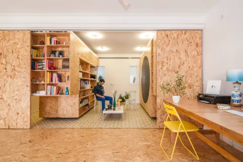 Ein Mann sitzt in einem Raum, der mit OSB-Platten für den Innenausbau gestaltet ist. Bücherregale und ein Schreibtisch sind ebenfalls aus OSB gefertigt.