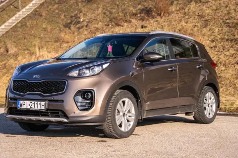 Brązowy Kia Sportage 2020 zaparkowany na drodze, z widocznymi schodami w tle.